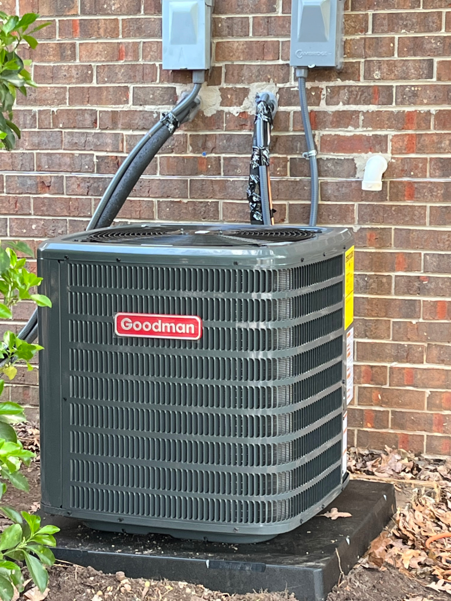 Outdoor Breeze installed residential AC condenser unit beside a brick home with new line set and disconnect boxes